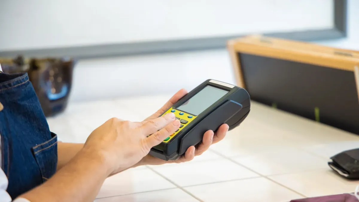Mão segurando maquininha de cartão para pagamento