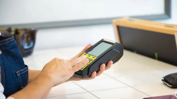Mão segurando maquininha de cartão para pagamento