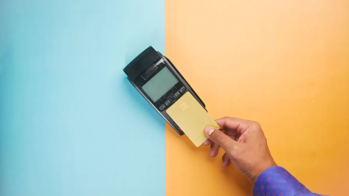 Mão aproximando cartão de crédito de terminal de pagamento